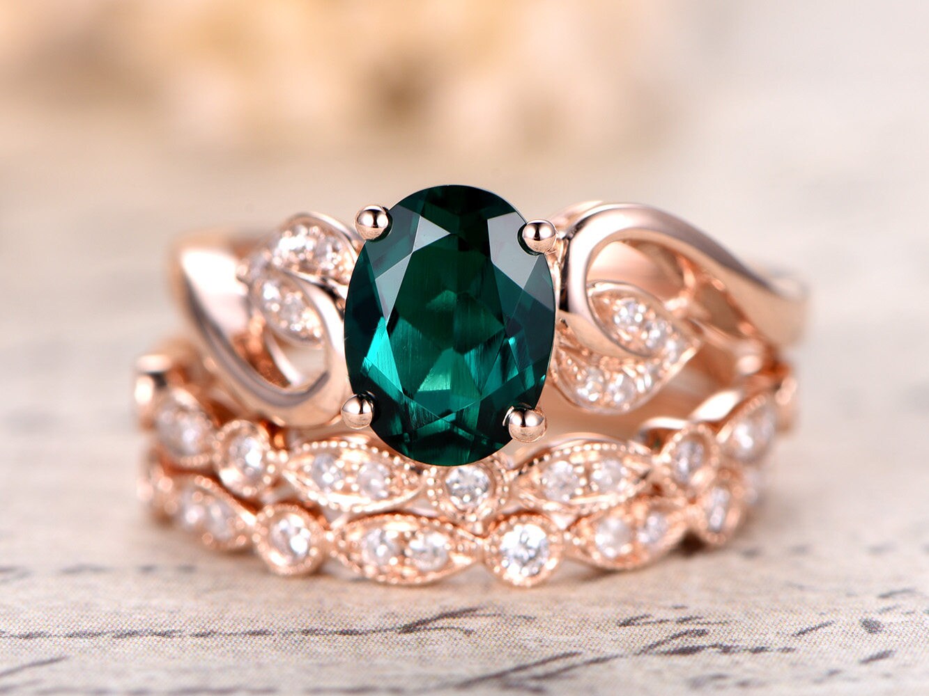 Ensemble de bague de fiançailles en or rose 14 carats comprenant une émeraude ovale et deux alliances perlées.